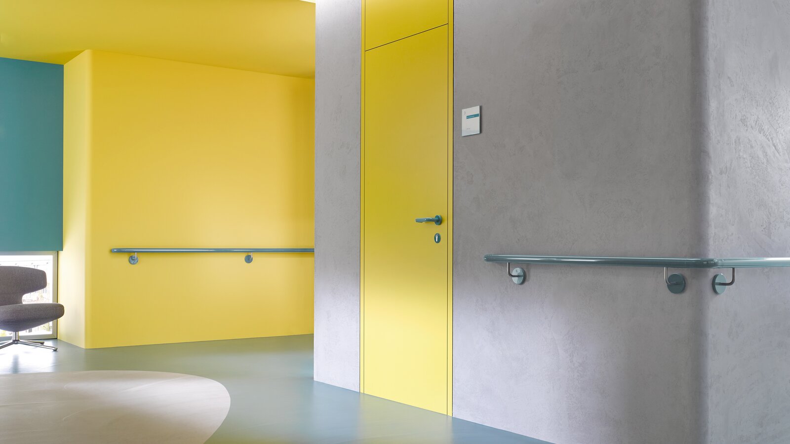 HEWI lever handle & handrail aqua blue Yellow hallway door equipped with System 111 lever handle in aqua blue and handrail in aqua blue