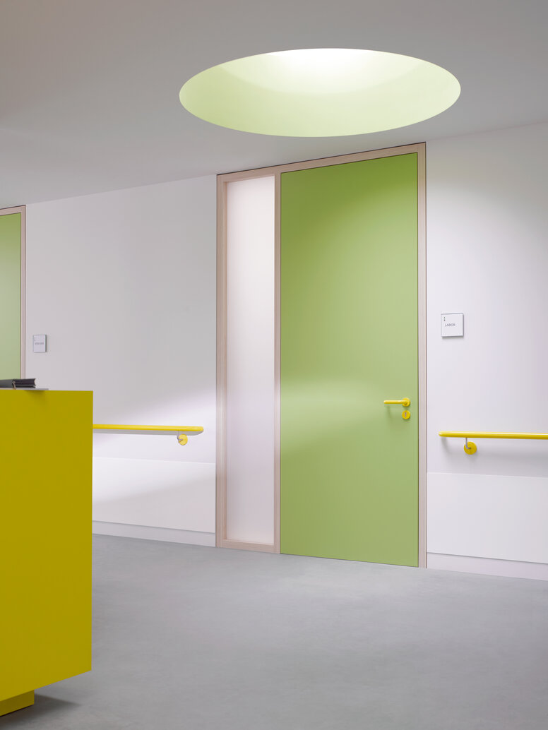 Green hallway door equipped with System 111 lever handle in the colour mustard yellow and handrail in the colour mustard yellow