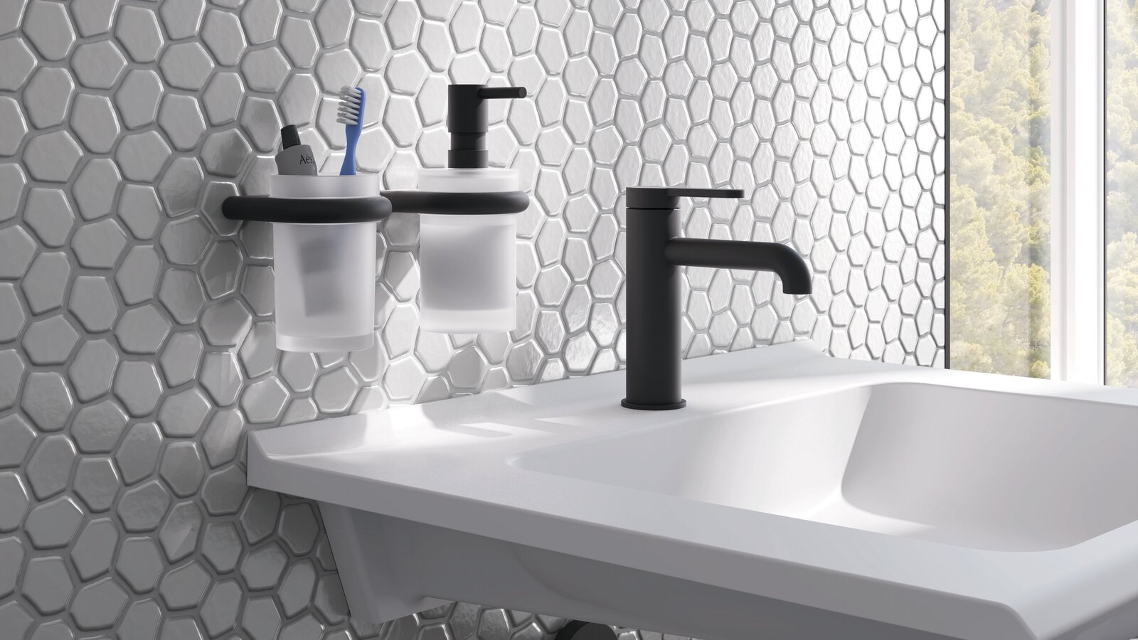 A white washbasin with a black tap and two wall-mounted cups in black holders against a backdrop of grey tiles