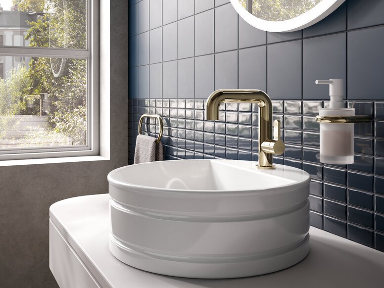 A modern washbasin with a gold-coloured tap, set against dark blue tiles and a large window letting in plenty of natural light