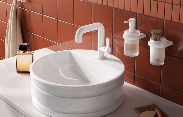 HEWI AQ11 fittings A round white countertop washbasin with a raised rim and a white tap, set on a light-coloured countertop against a backdrop of terracotta tiles