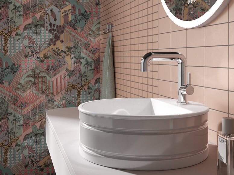 A round white countertop washbasin with a chrome-plated tap, set against light-coloured tiles and colourful patterned wallpaper