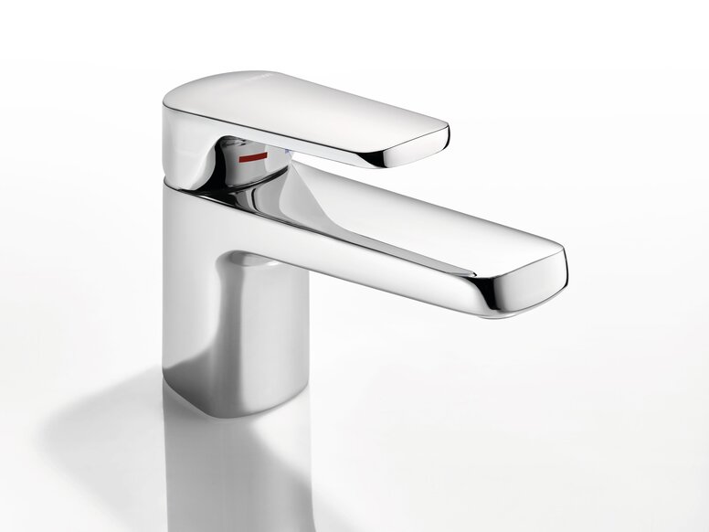 Chrome-plated tap with a short spout against a smooth white surface