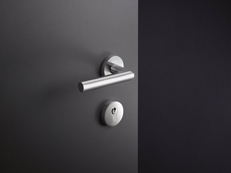 Door handle with a round rose and matching key escutcheon in stainless steel, with a smooth dark grey surface