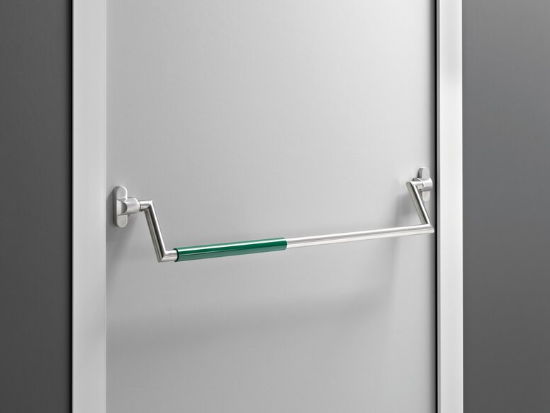 Stainless steel panic bar with a green grip section and two brackets on a white door with a frame