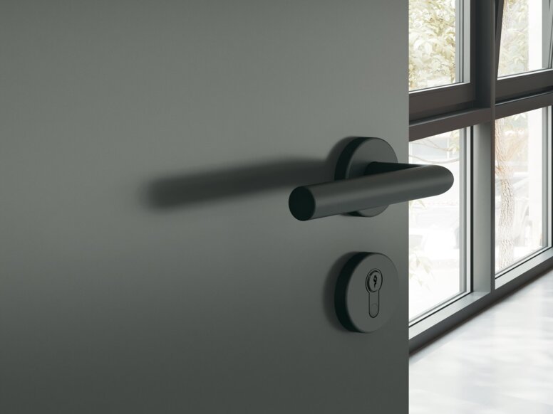HEWI System 162 Türdrücker Dunkelgraue pulverbeschichtete Türklinke mit runder Rosette an dunkelgrauer Tür, dahinter ein Arbeitszimmer mit Schreibtisch und Stuhl