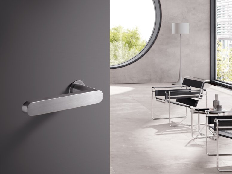 HEWI Serie 270 Türdrücker Türklinke aus Edelstahl an grauer Tür, dahinter heller Raum mit Stühlen