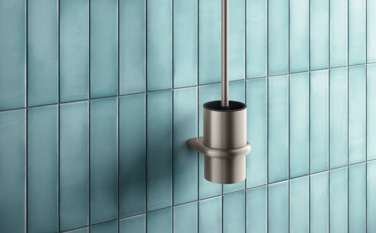Toilet brush and side-mounted toilet roll holder with a bronze-coloured PVD coating against a backdrop of blue tiles