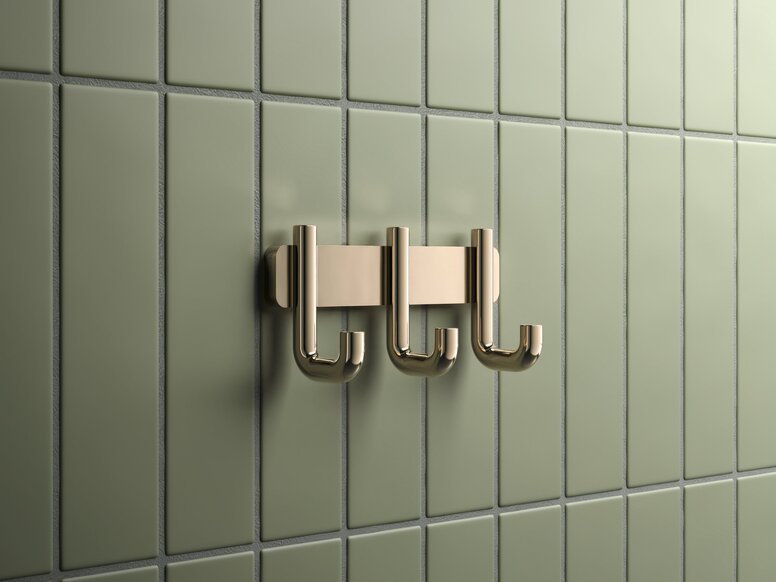 Triple hook rail with a brass-coloured PVD coating against a backdrop of green tiles