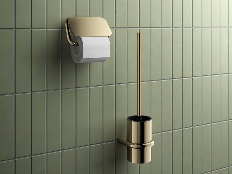 Toilet brush with a brass-coloured PVD coating and a matching toilet roll holder against a backdrop of green tiles