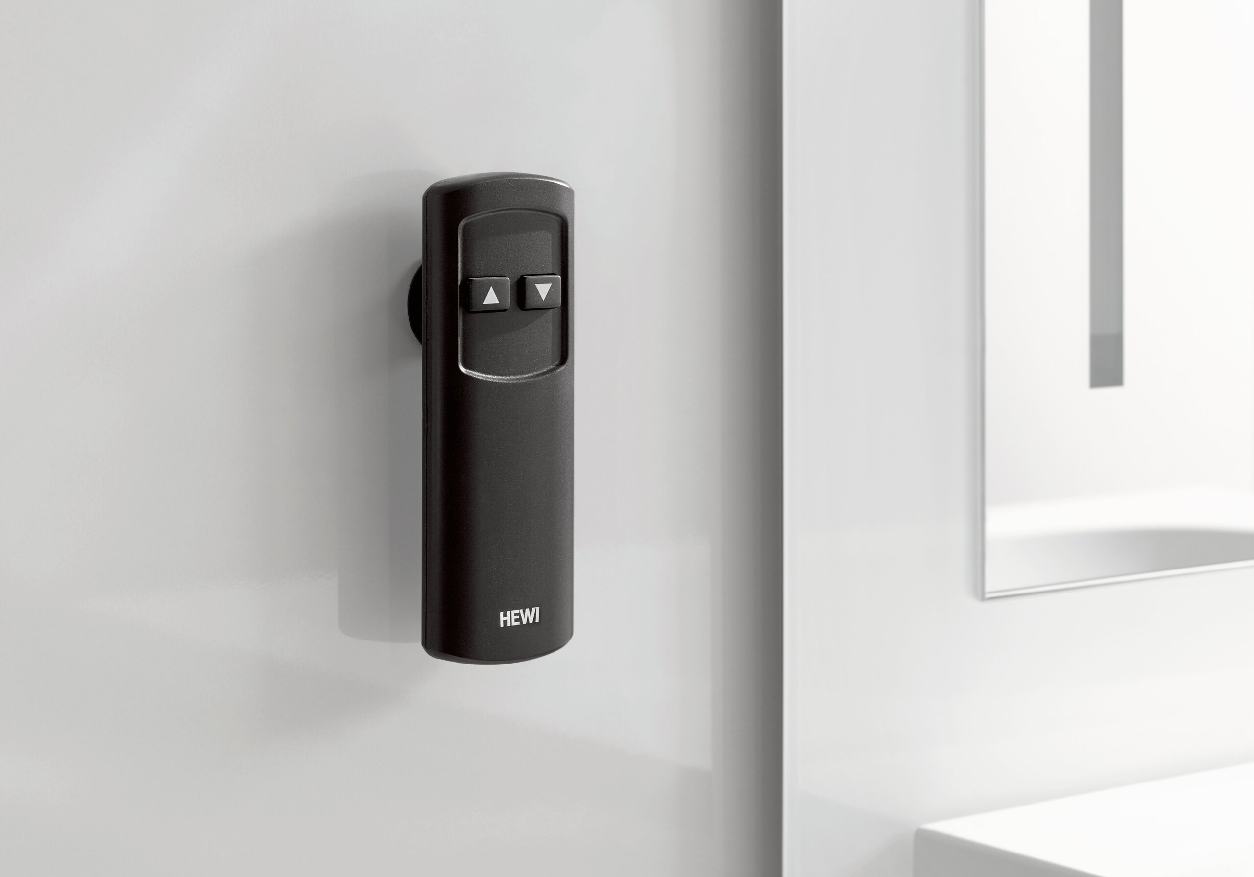 Black remote control with two arrow keys, shown against a light grey wall