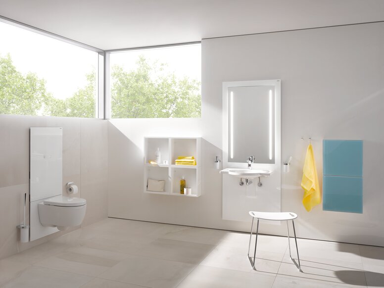 Weißes WC-Modul in einem hellen Badezimmer mit beleuchtetem Spiegel über dem Waschbecken, davor ein Hocker mit weißer Sitzfläche