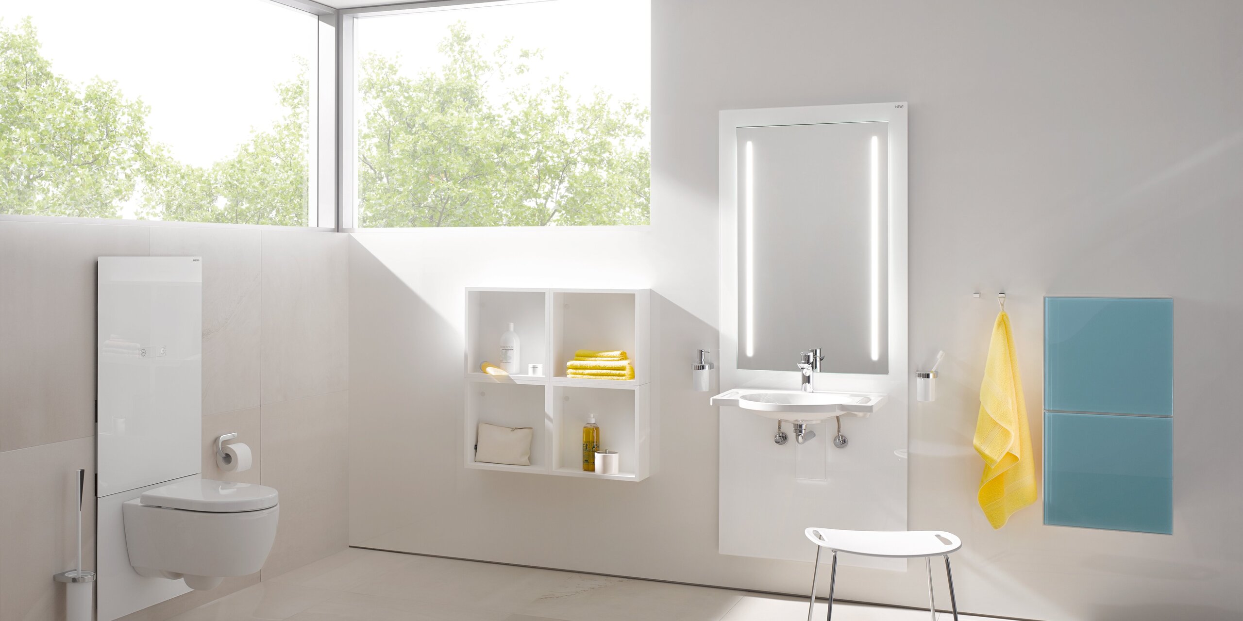 A white WC module in a bright bathroom with an illuminated mirror above the washbasin, in front of which stands a stool with a white seat
