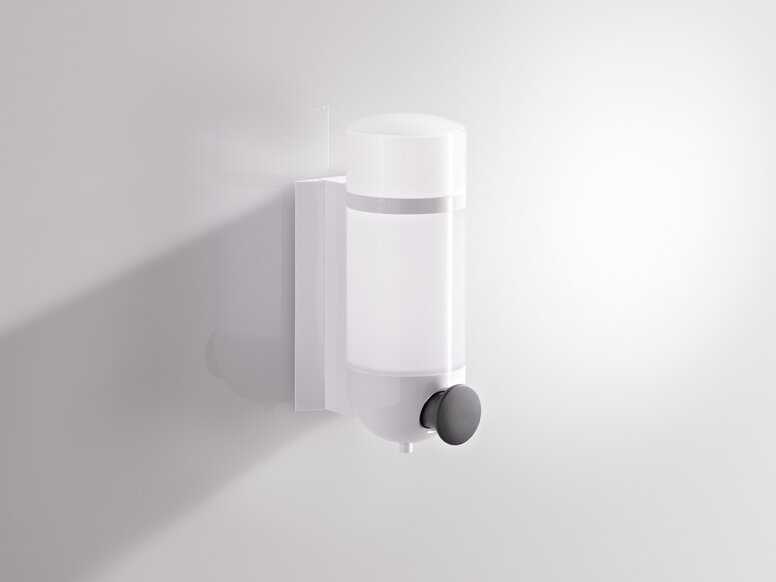 Synthetic material soap dispenser with a transparent container and a round pump in white and grey against a white wall