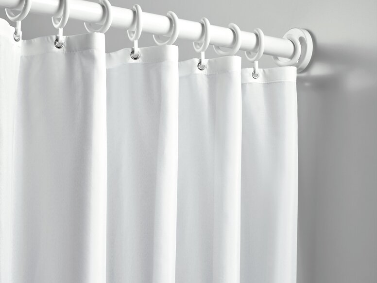 A shower curtain with white rings, hung on a white curtain rail against a light grey wall
