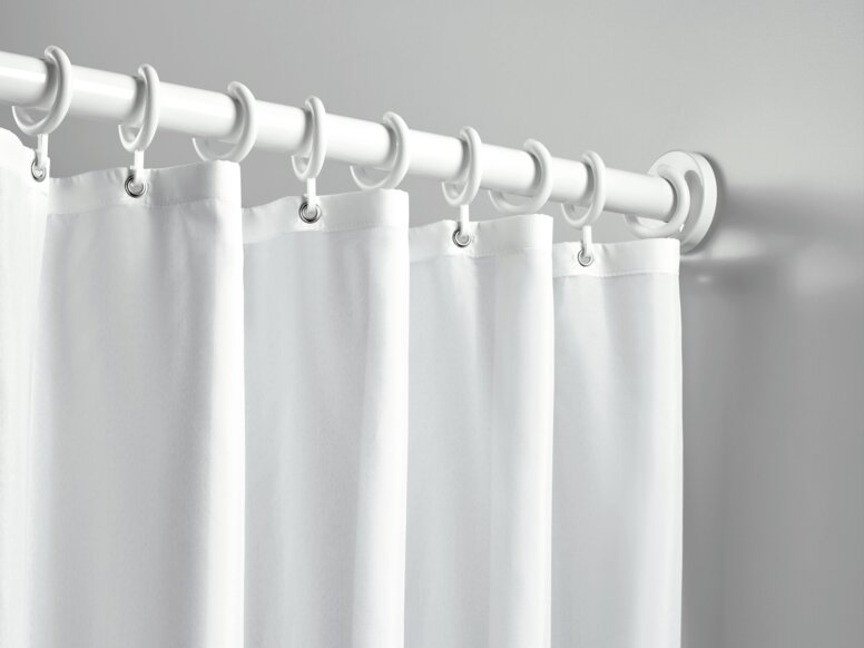A shower curtain with white rings, hung on a white curtain rail against a light grey wall