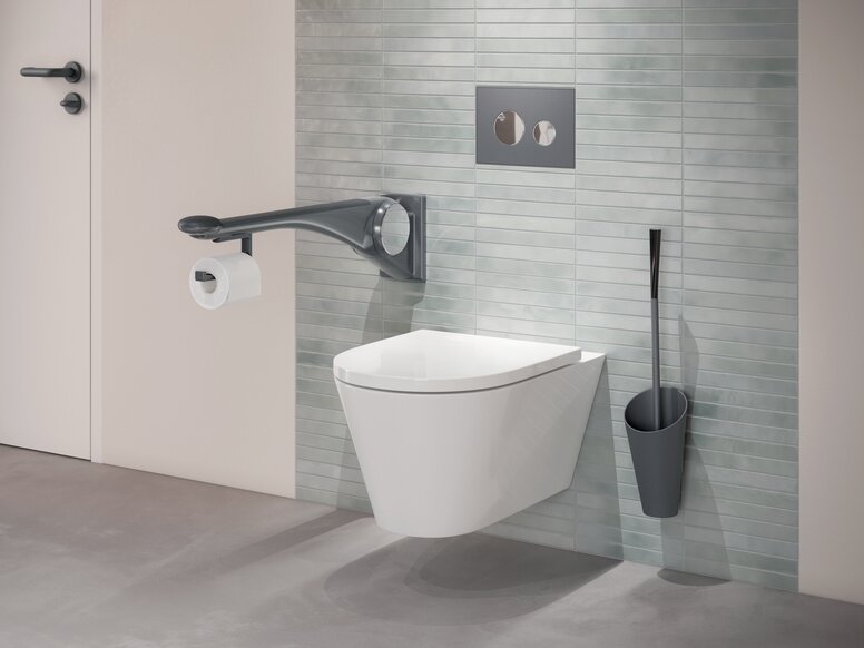 Wandhängendes WC mit seitlichem Haltegriff, integriertem WC-Papierhalter sowie einer an grüner Fliesenwand montierten Toilettenbürste