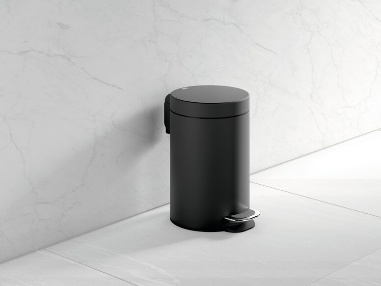 Black powder-coated bin with a foot pedal and a round cover, set against a white marble wall