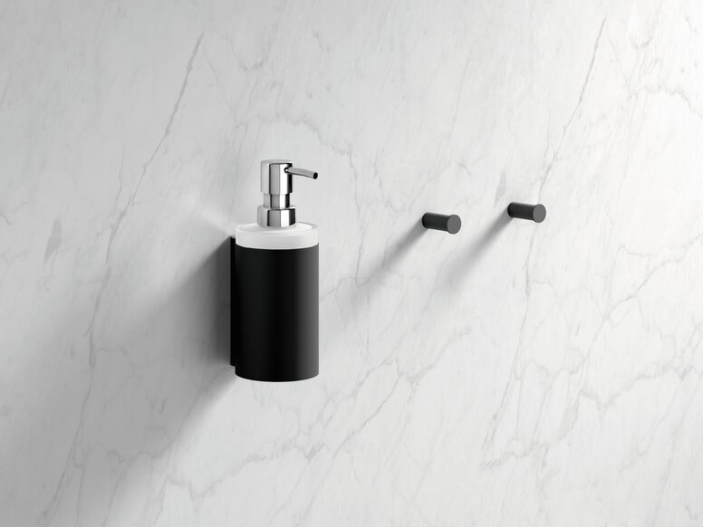 HEWI System 900 soap dispenser with holder and single hook Black powder-coated wall-mounted soap dispenser with a lever pump and two hooks, set against a white marble background