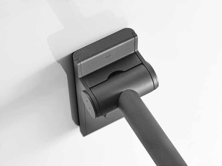 Close-up of the matt black hinge section of a Mono hinged support rail with a rectangular wall mounting plate and a rail extending diagonally downwards