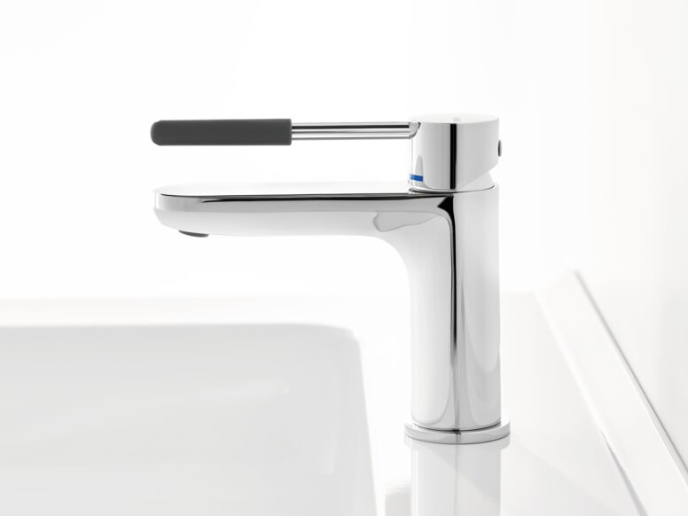 HEWI AQ single-lever washbasin mixer tap Chrome-plated tap with a long lever handle and dark grey grip sleeve on a white washbasin against a white background