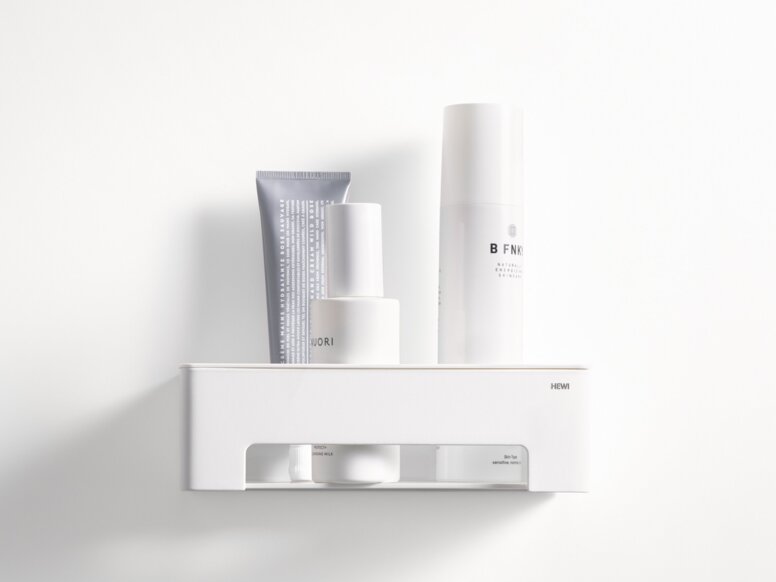 HEWI System 900 Duschkorb Weißer wandhängender Duschkorb mit Ablagefläche und offenem Fach, bestückt mit Pflegeprodukten an weißer Wand