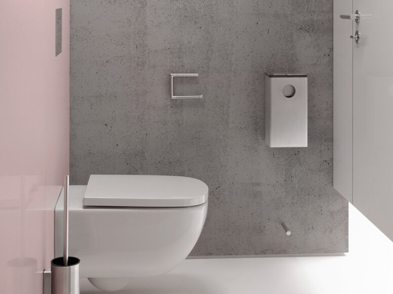 Schmaler WC-Bereich mit wandhängendem weißem WC vor einer grauen Wand in Betonoptik, weißem Toilettenpapierhalter und Toilettenbürstengarnitur sowie einer rosafarbenen Seitenwand