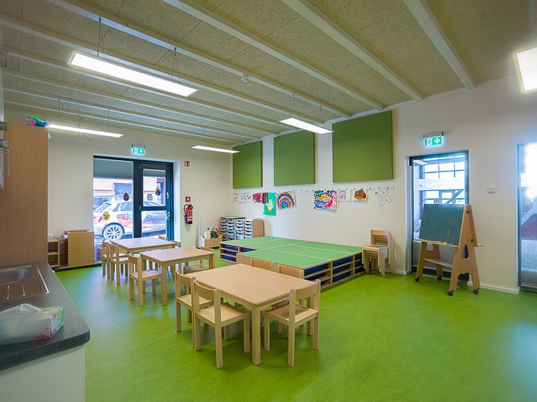 Group room of a daycare center with green floor and wooden tables and chairs